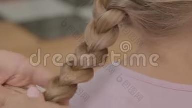 年轻女子的特写双手编织着她金发女儿的辫子。 母亲、儿童、<strong>单亲</strong>的概念